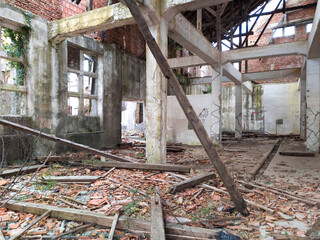 Demolished interior of a house. Rafters and shingles from the fallen roof strewn on the concrete floor and only the bare walls and construction frame left.