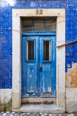 Blue aged double door made of wood on a house with azulejo facade. Empty clothes line is hanging above the entrance. In Lisbon Portugal.