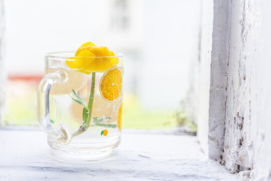 Still life high key, one globeflower in a glass cup in the water. Window in an old country house, white window sill and frame. Spring morning, natural light. A yellow flower. The first spring flowers.