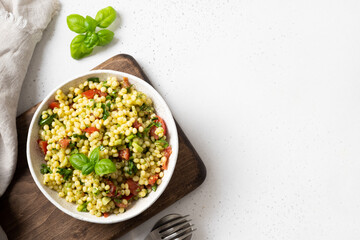 Pasta ptitim with vegetables, tomatoes, greens on white. Top view. Space for text.