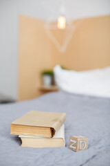 Stack of books and wooden brick with letters on a bed. Grey bedroom with wooden wall. Romantic evening with books. Reading with kids