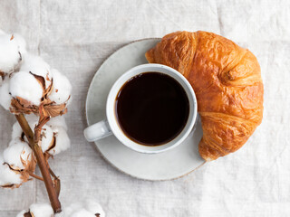 Cup of espresso coffee with croissant on a table with cotton branch.