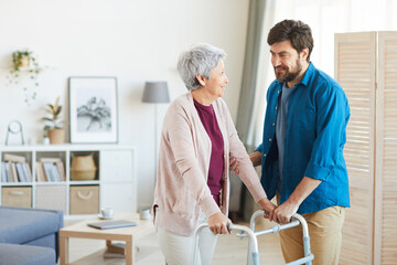 Mature bearded man caring about senior woman he helping her to walk around the room