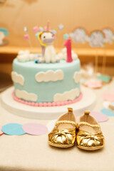 Little golden girl's booties on background of Birthday cake. First Birthday party. Little lady