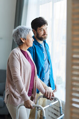 Older son taking care of his senior mother they standing near the window and talking at home