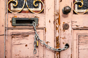 Vintage pink double door, paint peeling, closed and secured with metal chain passed through an empty keyhole and the mail slot. Abandoned, aged and empty house in need of restoration.