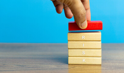 Hand holding red color woodblock on the wooden stack, conceptual with RISK word