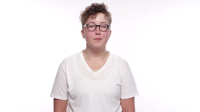 A young woman with short hair, glasses, and lip and nose ring smirks and smiles on a white studio background