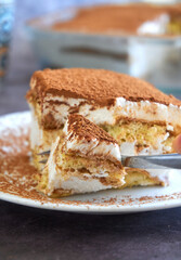 Cutting a square slice of Italian tiramisu cake with a fork, homemade gluten-free layered dessert with ladyfinger biscuit and mascarpone cream decorated with cocoa powder