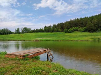 wooden bridge for swimming on the lake on a sunny day against a green forest on the other shore and a beautiful blue sky with clouds near the countryside