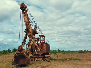 huge old excavator with peeling paint near a sand pit against a beautiful blue sky with clouds