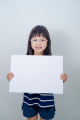 Obraz na płótnie Canvas Funny little girl holds a placard plate for inscriptions. Gray background
