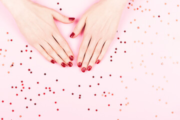 Manicure and nailcare concept. Two woman hands and falling confetti on pink background. Flat-lay, top view. Copy space.