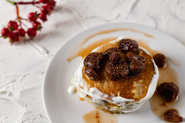 A stack of crumpets and pancakes with sour cream and strawberry sweet jam with berries on top of the dish. Dessert on a white plate with fruit in the background