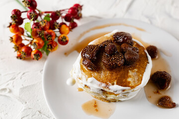 A stack of crumpets and pancakes with sour cream and strawberry sweet jam with berries on top of the dish. Dessert on a white plate with fruit in the background