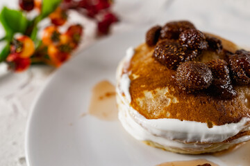 A stack of crumpets and pancakes with sour cream and strawberry sweet jam with berries on top of the dish. Dessert on a white plate with fruit in the background