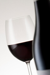 A glass of red wine with a bottle out of focus portruding in the foreground.