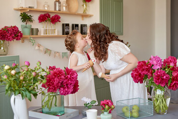 Mother's Day Greeting Card. Happy family, pregnant woman with little daughter in kitchen with peonies flowers. Relationship between parents and children. Motherhood, pregnancy, happiness concept.
