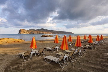 Empty beach with orange umbrellas and deck chairs closed. Beautiful summertime view seascape. 2020 summer quarantine travel. Relax places island Crete, Greece. Vacation cancellation, closed beaches.