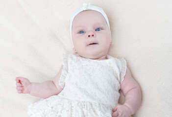 Cute little baby girl in white dress lying on bed top view