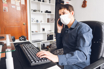 young man works from home in latinamerica  with the pc using mask, desktop in bedroom, in quarantine for coronavirus covid 19