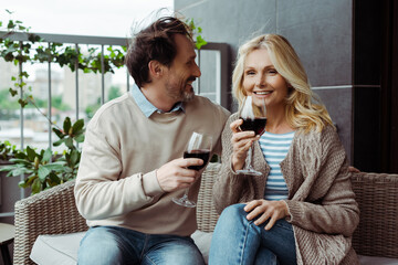 Handsome mature man looking at smiling wife with glass of wine on terrace