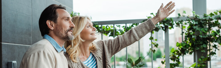 Panoramic crop of smiling woman pointing with hand near husband on terrace