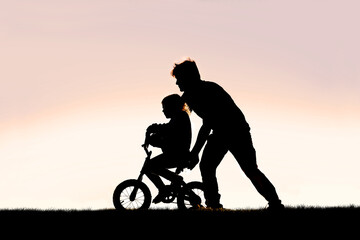 Fototapeta na wymiar Father Helping his Young Child Learn to Ride Bike with Training