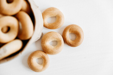 Drying or round bagels in a paper bag on a white wooden background. Top view. Copy, empty space for text
