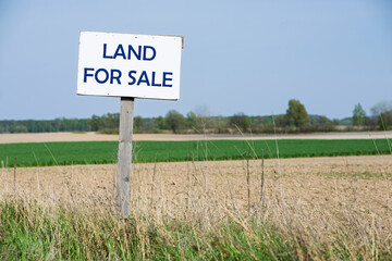A sign is in front of the land. For sale. Blue text.