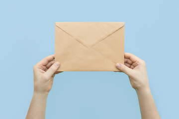 A man holding a craft brown envelope in hands on blue background. Receiving mail, sending letters