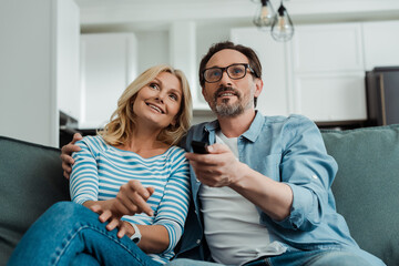 Selective focus of smiling mature couple watching tv on sofa