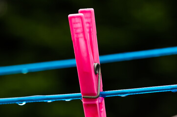 A blue clothing line with many raindrops at the string in front of a dark background, with a pink peg after the rain. Retro way of doing the laundry.