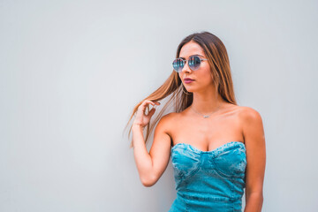 Lifestyle session, a young caucasian brunette in a blue denim dress and sunglasses on a plain gray background, with room for copy and paste, looking to the left
