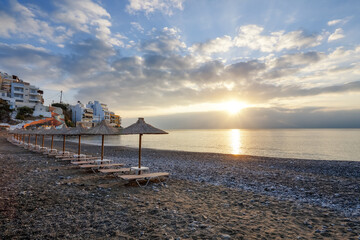 Fototapeta na wymiar Empty beach with umbrellas and deck chairs closed. Unbelievable sunrise. Beautiful summertime view seascape. 2020 summer quarantine travel. Relax places island Crete, Greece. Free space for text.