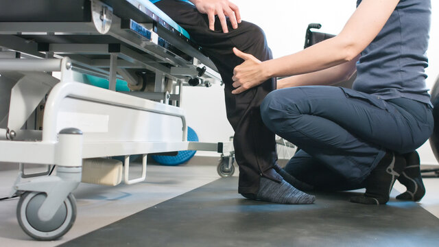 Physiotherapist exercising with disabled person using wheelchair on a therapy table.