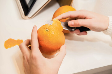 The girl's hands peel an orange with a knife. Preparing fruit salad for Breakfast.