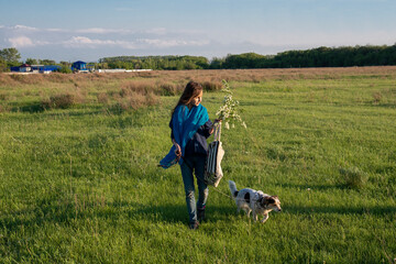 Girl with a dog walks in a green field.