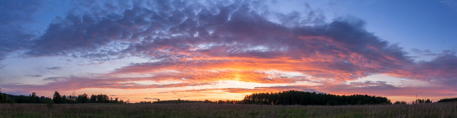 Sunset panoramic landscape of summer field under blue sky with clouds