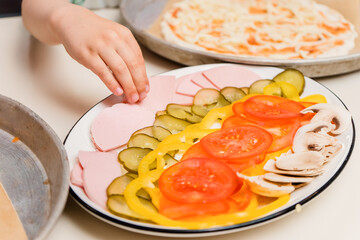 The child cooks. The hand reaches for the pizza filling. Kids' culinary class on baking