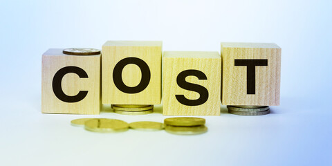 COST word written on wooden blocks on stacks of coins with white backround