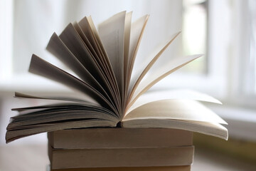 Stack of unrecognizable books on wooden table. Selective focus, natural window light.