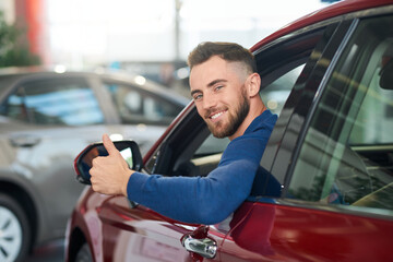 Smiling man showing thumb up in car.
