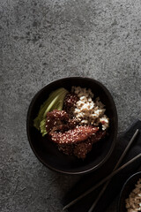 Lacquered chicken with sweet soy teriyaki sauce in a black bowl. Conditioned with rice. Some sticks and top view.