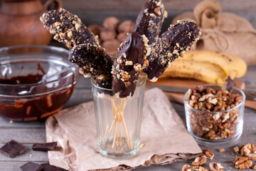 Frozen Chocolate Covered Bananas on a Stick in a glass beaker on wooden table