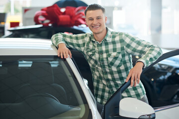Smiling man leaning on car in dealership.