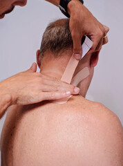 Naklejka premium Physiotherapist applying kinesio tape on the elderly man neck.