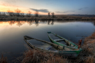 Two old boats on the river bank. Early morning. In the background, the sky is covered with clouds.