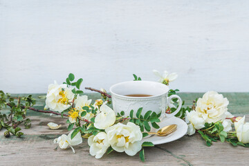 Romantic greeting card in retro style. White cup of coffee and white wild rose flowers on wooden background. Space for text