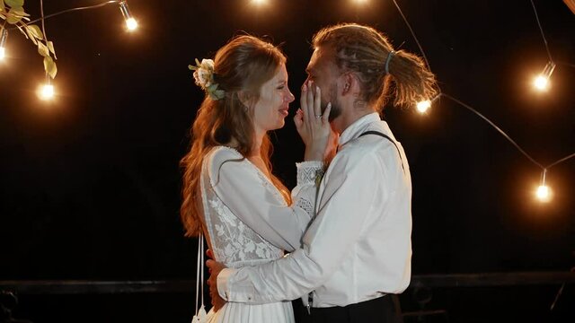 Tears of happiness of a sensual and emotional couple in love. The couple hugs, wipes each other's tears and kisses at night in the light of garlands on a warm summer night.